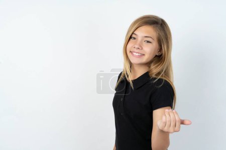 Foto de Hermosa chica adolescente caucásica con camiseta negra sobre la pared blanca invitando a venir con la mano. Feliz de que hayas venido. - Imagen libre de derechos