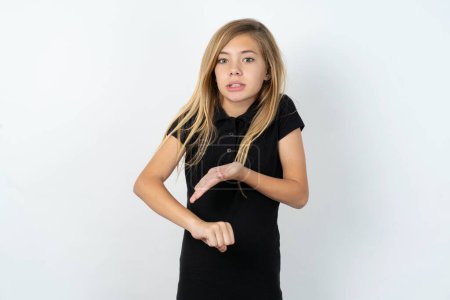 Téléchargez les photos : Belle caucasienne adolescent fille portant noir T-shirt sur blanc mur pressé pointant pour regarder le temps, impatience, bouleversé et en colère pour délai - en image libre de droit