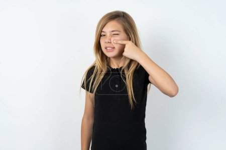 Téléchargez les photos : Belle adolescente caucasienne portant un T-shirt noir sur un mur blanc pointant malheureux à boutons sur le front, infection laide de la tête noire. Acné et problème de peau - en image libre de droit