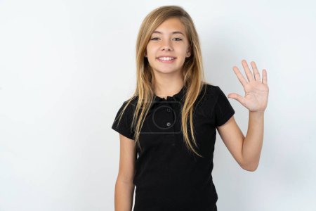 Photo for Beautiful caucasian teen girl wearing black T-shirt over white wall showing and pointing up with fingers number five while smiling confident and happy - Royalty Free Image