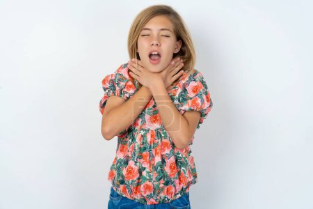 Foto de Hermosa chica adolescente caucásica con una blusa floreada sobre la pared blanca gritando sofocar porque estrangulamiento doloroso. Problema de salud. Concepto de asfixia y suicidio. - Imagen libre de derechos