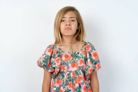 Photo for Shot of pleasant looking beautiful caucasian teen girl wearing flowered blouse over white wall, pouts lips, looks at camera, Human facial expressions - Royalty Free Image