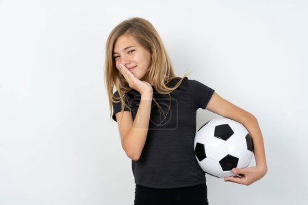 Foto de Chica adolescente muy alegre con ropa deportiva sosteniendo una pelota de fútbol sobre la pared blanca se ríe alegremente y mantiene las palmas presionadas juntas oye algo divertido - Imagen libre de derechos