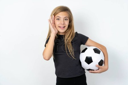Photo for Teen girl wearing sportswear holding a football ball over white wall Pleasant looking cheerful, Happy reaction - Royalty Free Image