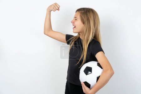 Photo for Profile photo of teen girl wearing sportswear holding a football ball over white wall supporting soccer team World Cup 2022 raise fist shouting - Royalty Free Image