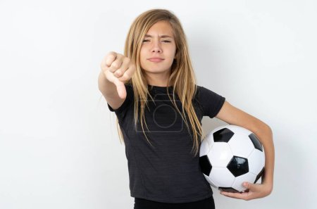 Téléchargez les photos : Adolescent fille portant des vêtements de sport tenant un ballon de football sur le mur blanc regardant malheureux et en colère montrant rejet et négatif avec les pouces vers le bas geste. Mauvaise expression. - en image libre de droit