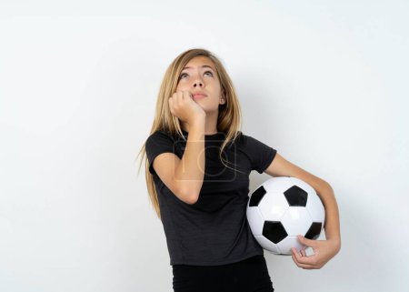 Foto de Retrato de chica adolescente triste usando ropa deportiva sosteniendo una pelota de fútbol sobre la pared blanca manos cara mirada espacio vacío - Imagen libre de derechos