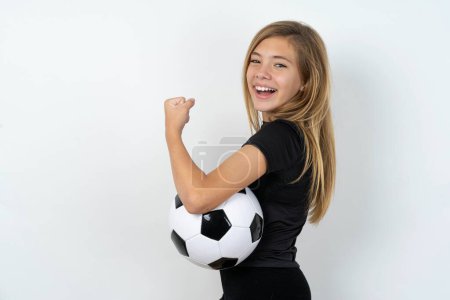 Photo for Profile side view portrait of teen girl wearing sportswear holding a football ball over white wall  celebrates victory - Royalty Free Image