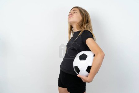 Photo for Teen girl wearing sportswear holding a football ball over white wall got back pain - Royalty Free Image