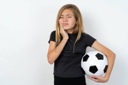 Foto de Adolescente chica usando ropa deportiva celebración de una pelota de fútbol sobre blanco pared con dolor de muelas sobre fondo blanco - Imagen libre de derechos