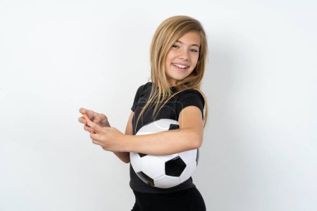 Photo for Nice addicted cheerful teen girl wearing sportswear holding a football ball over white wall using gadget playing network game - Royalty Free Image