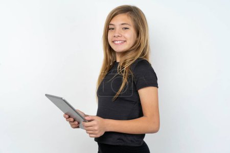 Foto de Foto de chica adolescente optimista caucásica con camiseta negra sosteniendo la tableta - Imagen libre de derechos