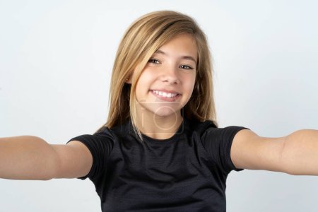 Téléchargez les photos : Photo de belle adolescente caucasienne portant un t-shirt noir faisant du selfie sur fond blanc - en image libre de droit