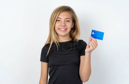 Photo for Photo of happy cheerful smiling positive caucasian teen girl wearing black T-shirt over white wall recommend credit card - Royalty Free Image