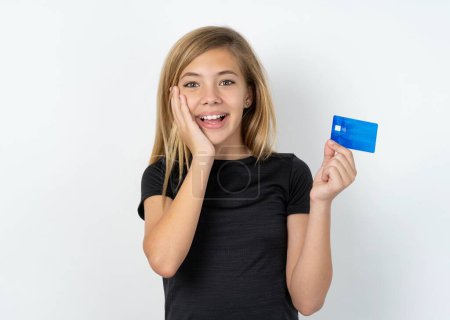 Foto de Sorprendido positivo caucásico adolescente chica usando negro camiseta sobre blanco pared brazo cara hold banco plástico tarjeta impresionado funciones - Imagen libre de derechos