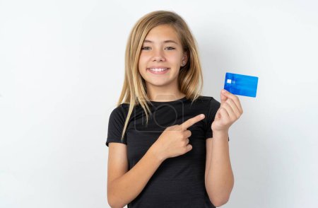 Foto de Foto retrato de chica adolescente caucásica sobre pared blanca haciendo la compra con el dedo de la tarjeta bancaria de crédito - Imagen libre de derechos