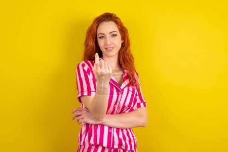 Téléchargez les photos : Jeune femme aux cheveux rouges portant un pyjama rose sur fond jaune studio signe de venir ici geste avec la main invitant accueillant heureux et souriant - en image libre de droit