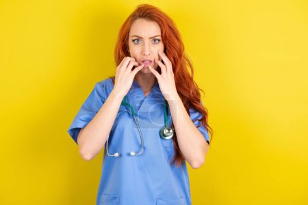 Photo for Speechless young red-haired doctor woman over yellow studio background keeps hands near opened mouth reacts to shocking news stares wondered at camera - Royalty Free Image