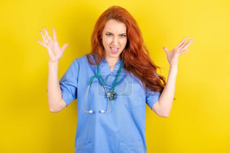 Photo for Crazy and outraged red-haired doctor woman over yellow studio background screams loudly and gestures angrily yells furiously. Negative human emotions feelings concept - Royalty Free Image