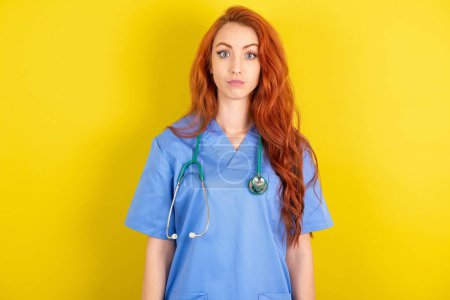 Photo for Stunned young red-haired doctor woman over yellow studio background stares reacts on shocking news. Astonished woman holds breath - Royalty Free Image