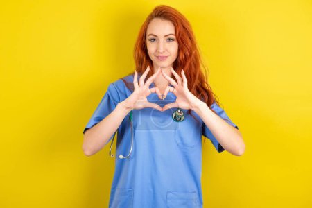 Téléchargez les photos : Sérieux jeune femme médecin aux cheveux roux sur fond jaune studio garde les mains croisées se tient dans la pose réfléchie concentrée quelque part - en image libre de droit
