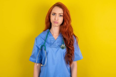 Photo for Displeased young red-haired doctor woman over yellow studio background frowns face feels unhappy has some problems. Negative emotions and feelings concept - Royalty Free Image