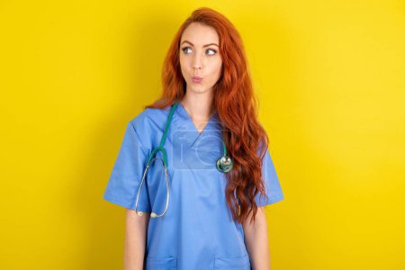 Photo for Shocked young red-haired doctor woman over yellow studio background look empty space with open mouth screaming: Oh My God! I can't believe this. - Royalty Free Image
