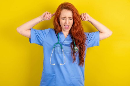 Photo for Photo of crazy young red-haired doctor woman over yellow studio background screaming and pointing with fingers at hair closed eyes - Royalty Free Image