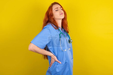 Photo for Young red-haired doctor woman over yellow studio background got back pain - Royalty Free Image
