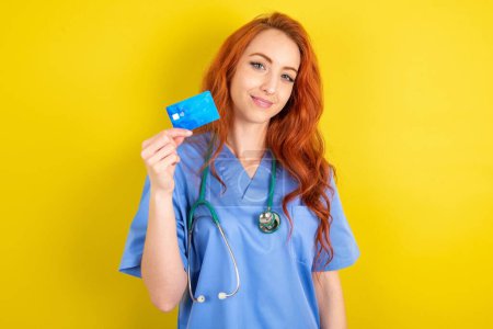 Photo for Close up photo of optimistic young red-haired doctor woman over yellow studio background hold card - Royalty Free Image