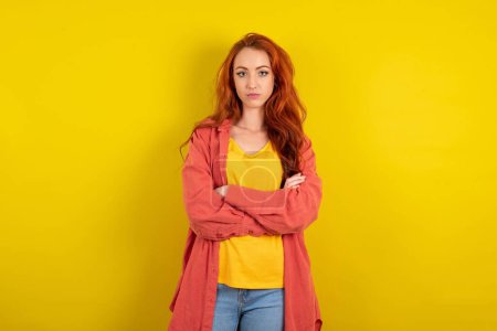 Téléchargez les photos : Femme aux cheveux rouges sérieux et coûteux debout sur fond jaune studio se sentent comme cool entrepreneur confiant mains croisées. - en image libre de droit