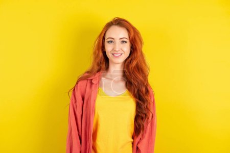 Foto de Foto de cerca de una hermosa mujer pelirroja de pie sobre el fondo amarillo del estudio con una sonrisa dentada - Imagen libre de derechos