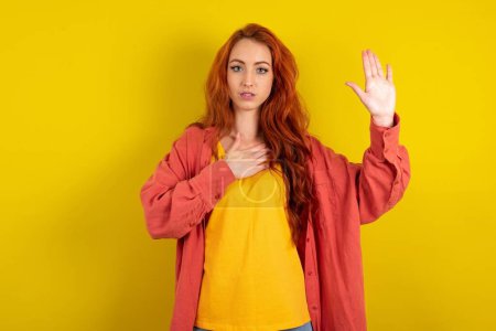 Photo for Beautiful red haired woman standing over yellow studio background Swearing with hand on chest and open palm, making a loyalty promise oath - Royalty Free Image