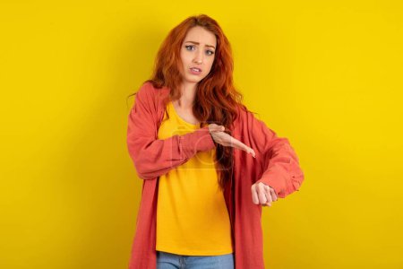 Téléchargez les photos : Belle femme aux cheveux roux debout sur fond de studio jaune pressé pointant vers regarder le temps, impatience, bouleversé et en colère pour retard de délai. - en image libre de droit