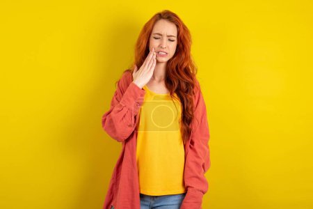 Photo for Beautiful red haired woman standing over yellow studio background touching mouth with hand with painful expression because of toothache or dental illness on teeth. - Royalty Free Image