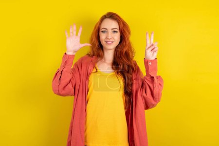 Photo for Beautiful red haired woman standing over yellow studio background showing and pointing up with fingers number seven while smiling confident and happy. - Royalty Free Image