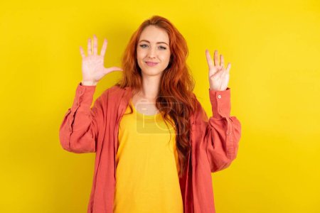 Téléchargez les photos : Femme aux cheveux rouges debout sur fond jaune studio montrant et pointant vers le haut avec les doigts numéro neuf tout en souriant confiant et heureux. - en image libre de droit