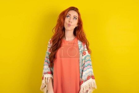 Téléchargez les photos : Femme aux cheveux roux debout sur fond jaune studio faisant visage de poisson avec des lèvres, geste fou et comique. Drôle d'expression. - en image libre de droit