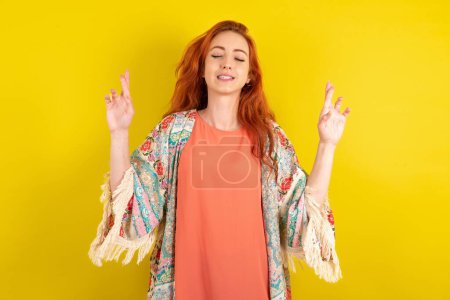 Photo for Red haired woman standing over yellow studio background gesturing finger crossed smiling with hope and eyes closed. Luck and superstitious concept. - Royalty Free Image