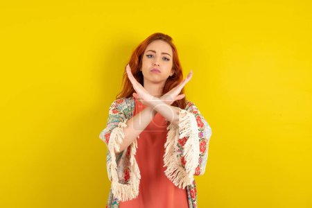 Téléchargez les photos : Femme rousse debout sur fond de studio jaune avec expression de rejet croisant les bras faisant signe négatif, visage en colère - en image libre de droit