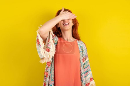 Photo for Red haired woman standing over yellow studio background smiling and laughing with hand on face covering eyes for surprise. Blind concept. - Royalty Free Image