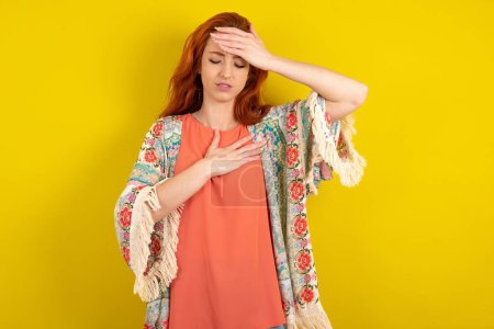 Téléchargez les photos : Femme rousse debout sur fond jaune studio Toucher le front pour la maladie et la fièvre, grippe et rhume, virus malade. - en image libre de droit