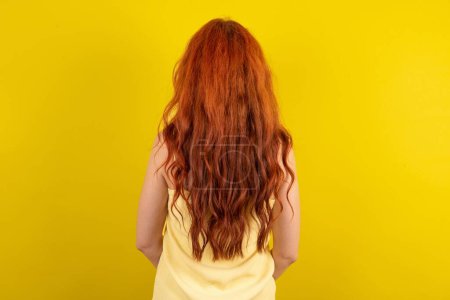 Téléchargez les photos : La vue arrière d'une belle femme aux cheveux rouges portant une chemise jaune sur fond de studio jaune. Studio Shoot. - en image libre de droit