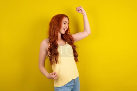 Photo for Profile photo of excited beautiful red haired woman wearing yellow shirt over yellow studio background  good mood raise fists screaming rejoicing overjoyed basketball sports fan supporter - Royalty Free Image