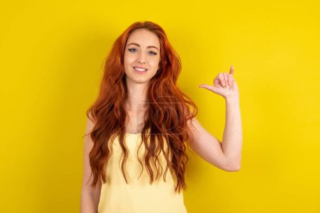 Photo for Beautiful red haired woman wearing yellow shirt over yellow studio background showing up number six Liu with fingers gesture in sign Chinese language - Royalty Free Image