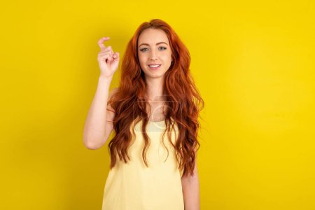Téléchargez les photos : Belle femme aux cheveux rouges portant chemise jaune sur fond studio jaune pointant vers le haut avec les doigts numéro neuf en langue des signes chinoise Jiu - en image libre de droit