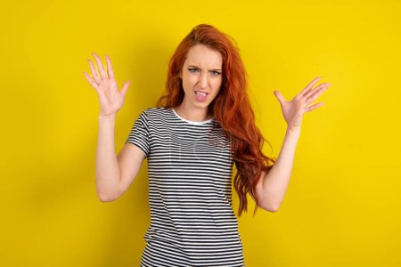 Photo for Crazy outraged red haired woman wearing striped shirt over yellow studio background screams loudly and gestures angrily yells furiously. Negative human emotions feelings concept - Royalty Free Image
