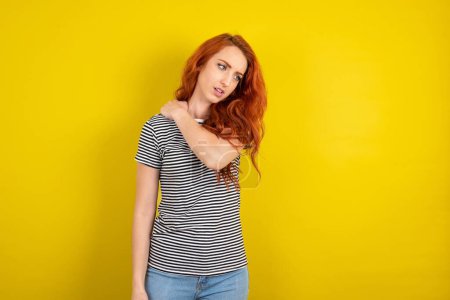 Foto de Mujer de pelo rojo con camisa a rayas sobre fondo de estudio amarillo tienen dolor de espalda - Imagen libre de derechos