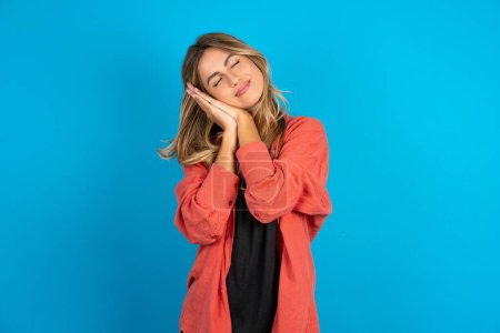 Photo for Blonde woman wearing overshirt  sleeping tired dreaming and posing with hands together while smiling with closed eyes. - Royalty Free Image
