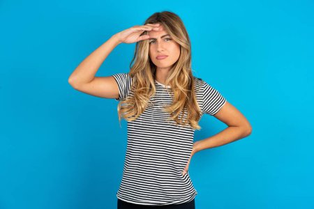 Photo for Young beautiful woman wearing striped t-shirt over blue background having problems, worried and stressed holds hand on forehead. - Royalty Free Image
